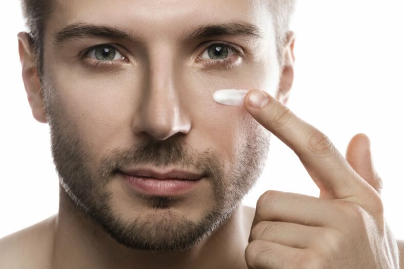 Verletzliche_Maennerhaut.jpg Ein Mann trägt eine Creme auf seine Wange auf, während er in die Kamera schaut. Hintergrund ist neutral.