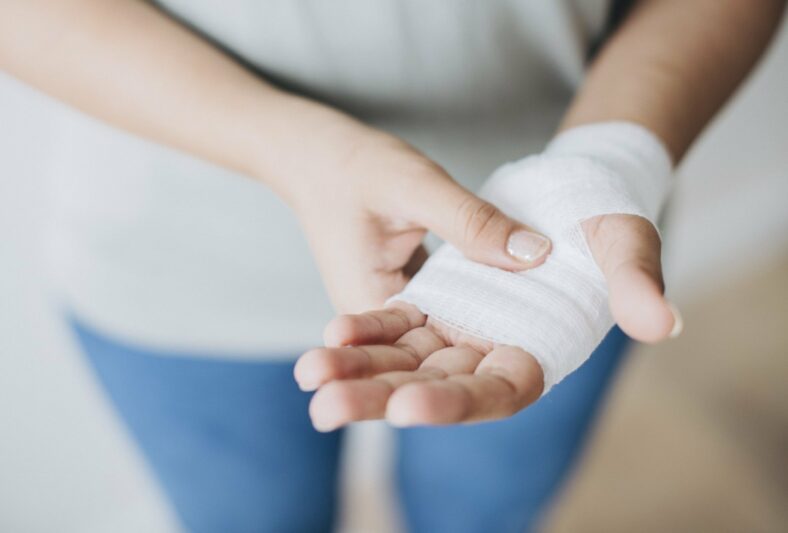 Wann_muessen_Verletzungen_aerztlich_versorgen__Gross_.jpg Händedetail mit einer verbundenen Hand, die eine sanfte Verletzung zeigt, während die andere Hand sie festhält.