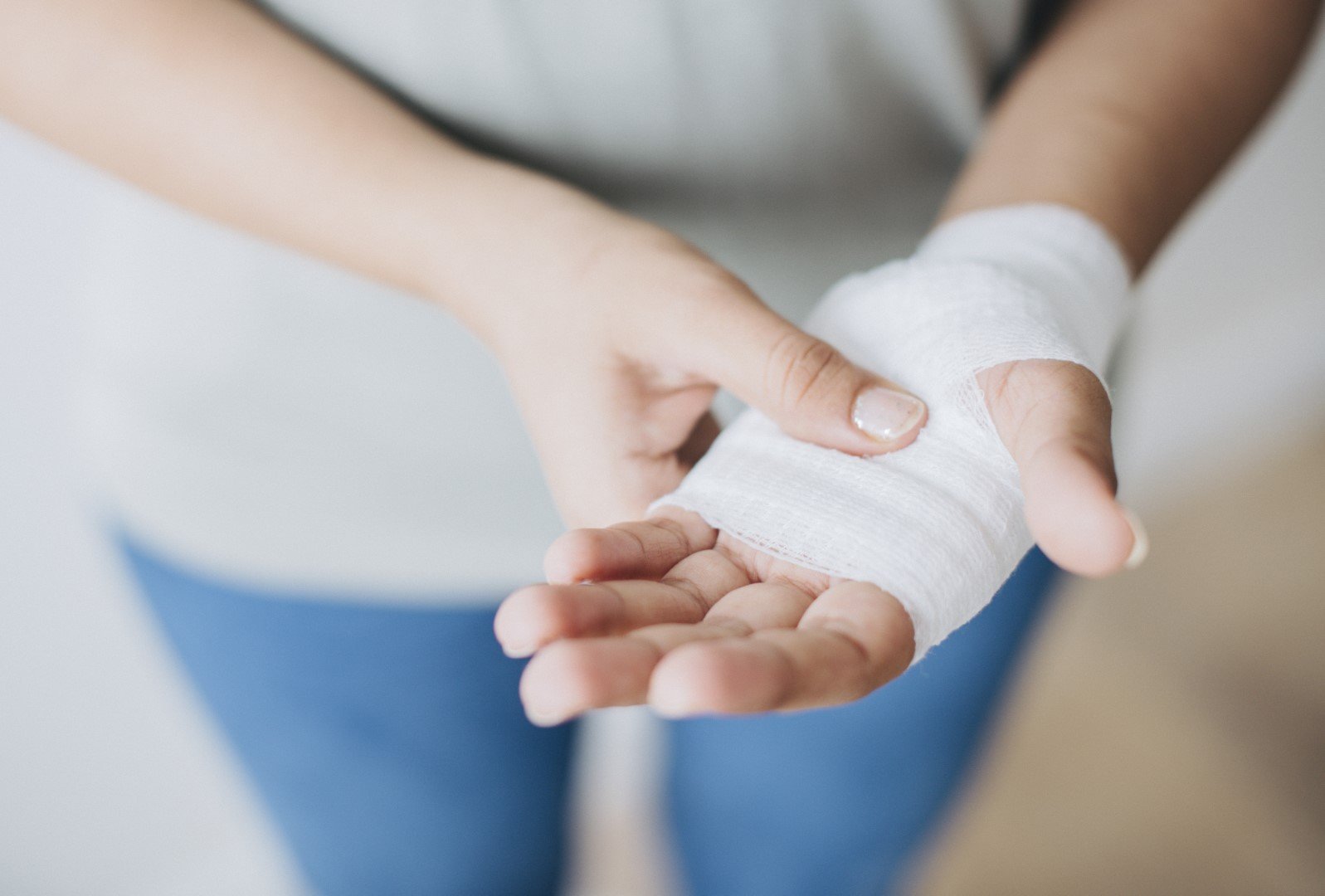 Wann_muessen_Verletzungen_aerztlich_versorgen__Gross_.jpg Händedetail mit einer verbundenen Hand, die eine sanfte Verletzung zeigt, während die andere Hand sie festhält.