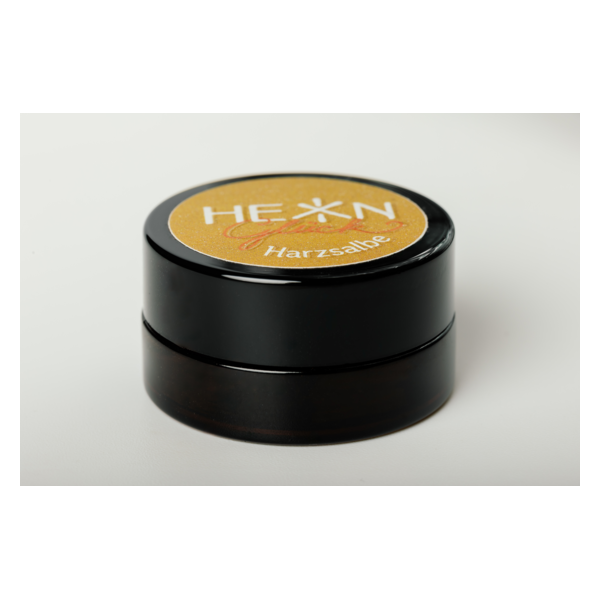 Runde schwarze Verpackung mit goldenem Deckel, beschriftet mit "HEXN Harzsalbe".