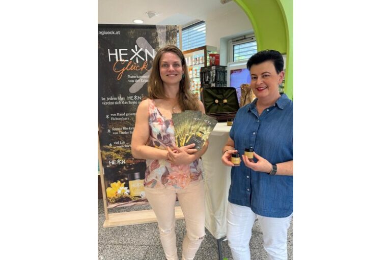 Zwei Frauen präsentieren Naturkosmetikprodukte von HEXN Glück, umgeben von Werbematerialien und einem Verkaufsstand.